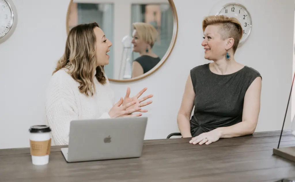 Two women sitting at a table in an office in deep discussion.